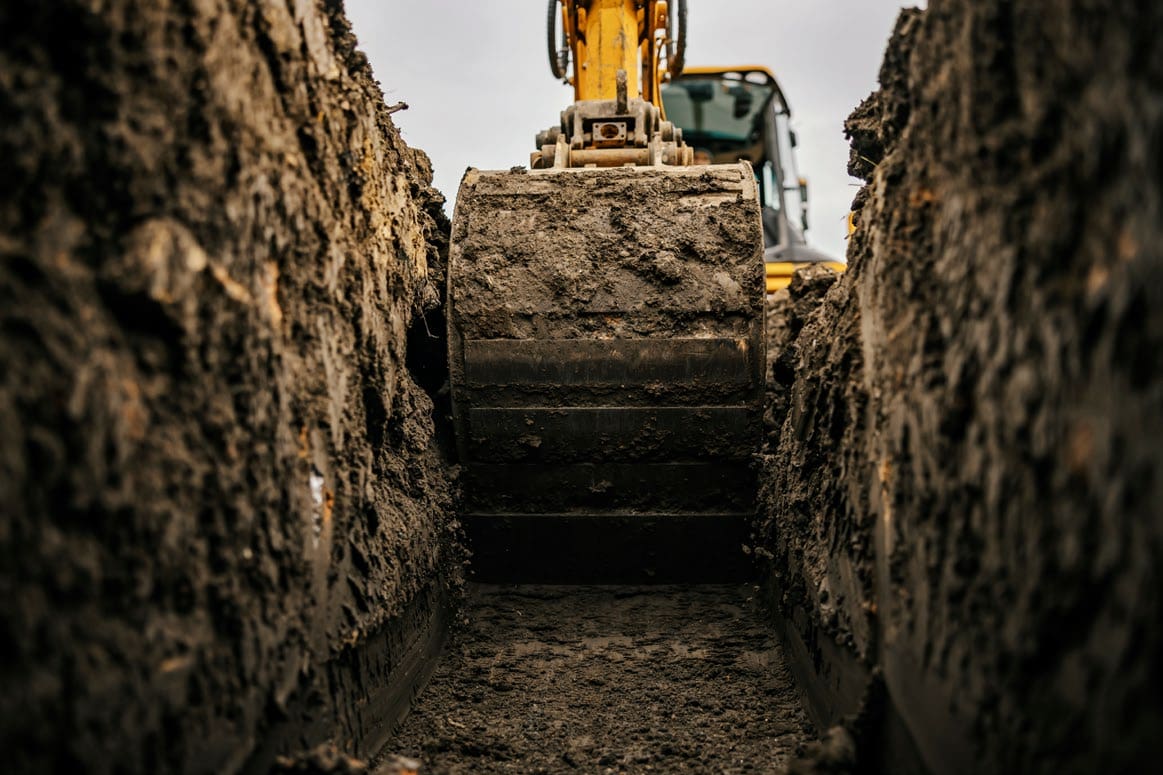 Excavator digging a deep muddy trench.
